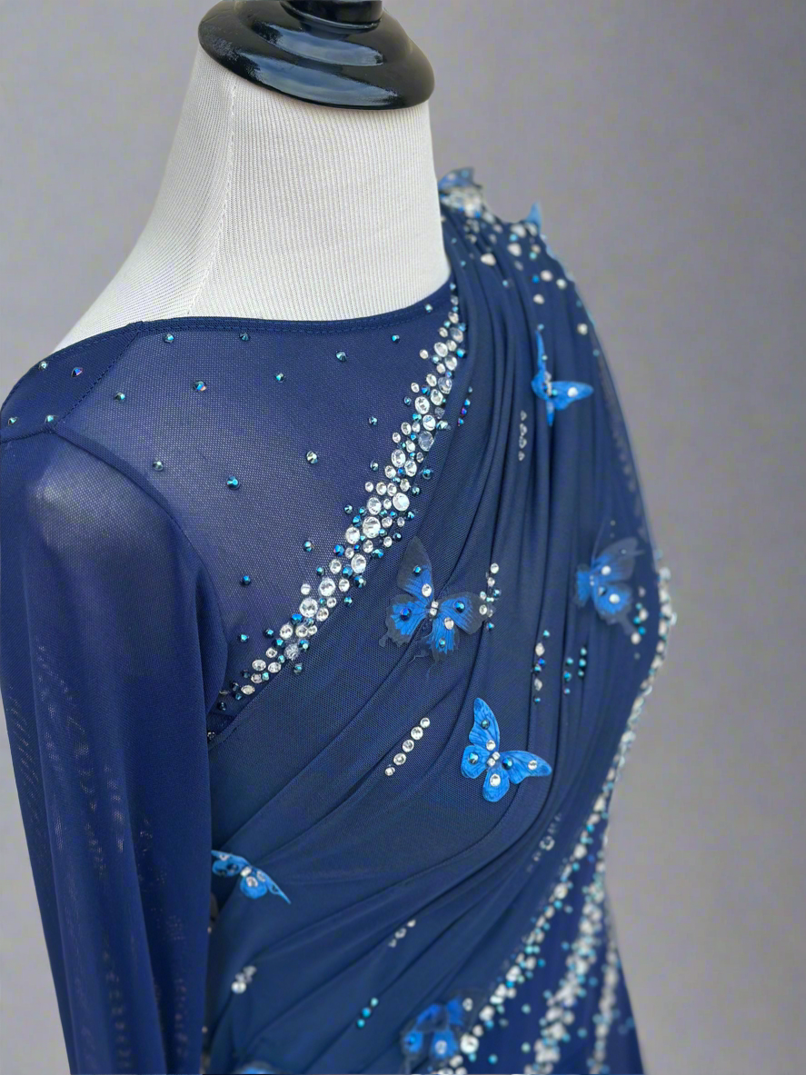 Elegant butterfly figure skating dress in deep blue with crystals, draped design, and open back – sparkle on ice.
