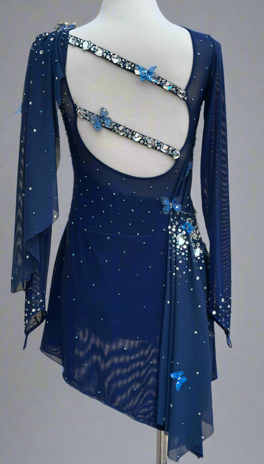 Elegant butterfly figure skating dress in deep blue with crystals, draped design, and open back – sparkle on ice.