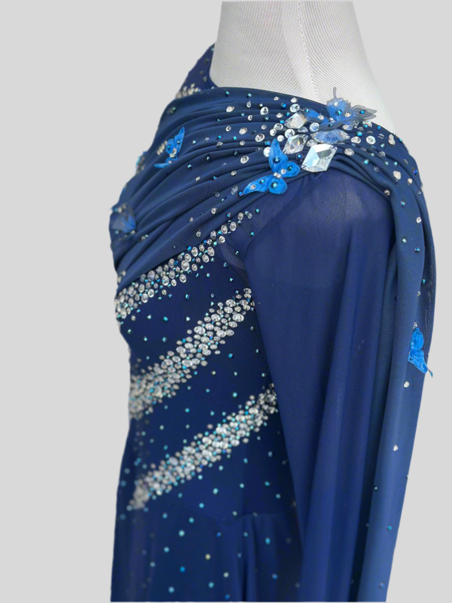 Elegant butterfly figure skating dress in deep blue with crystals, draped design, and open back – sparkle on ice.