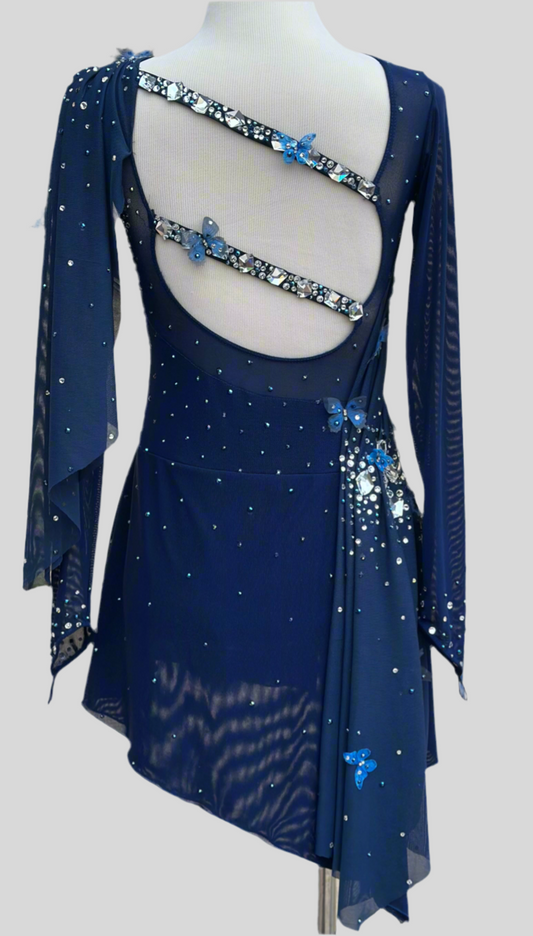 Elegant butterfly figure skating dress in deep blue with crystals, draped design, and open back – sparkle on ice.