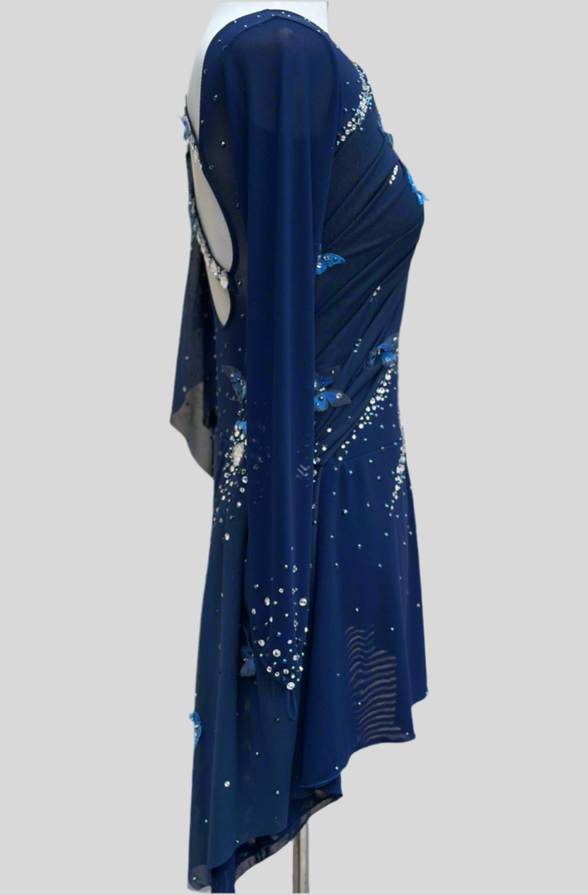 Elegant butterfly figure skating dress in deep blue with crystals, draped design, and open back – sparkle on ice.