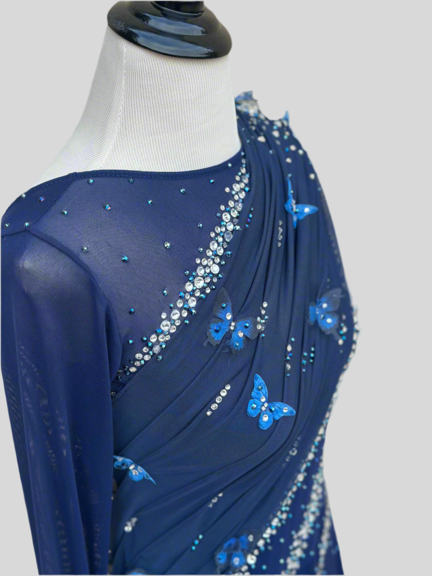 Elegant butterfly figure skating dress in deep blue with crystals, draped design, and open back – sparkle on ice.