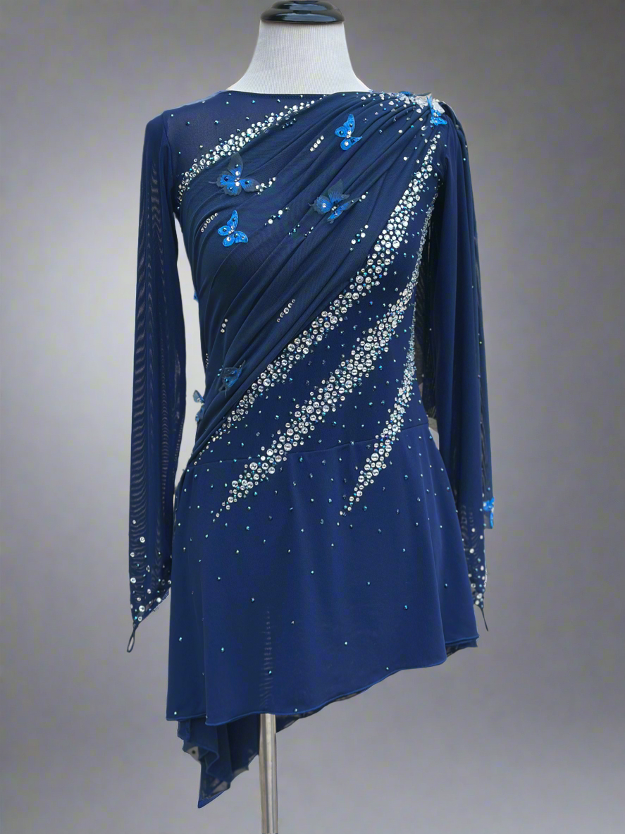 Elegant butterfly figure skating dress in deep blue with crystals, draped design, and open back – sparkle on ice.