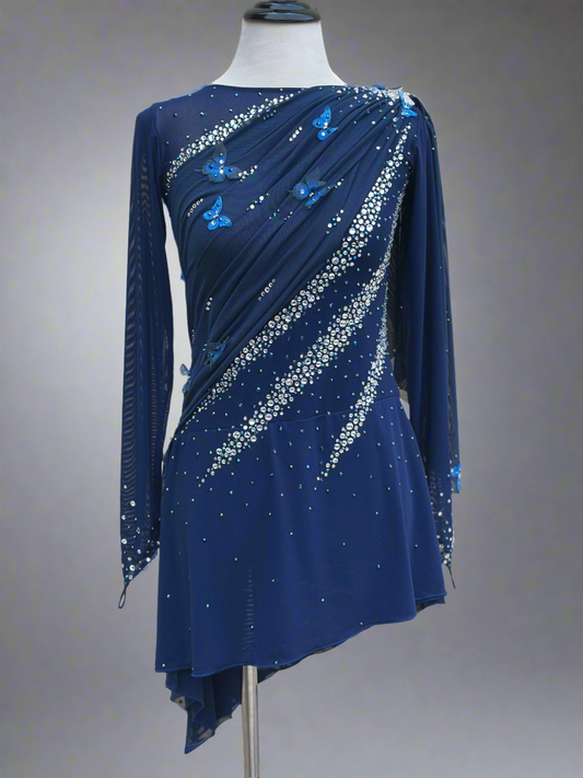 Elegant butterfly figure skating dress in deep blue with crystals, draped design, and open back – sparkle on ice.