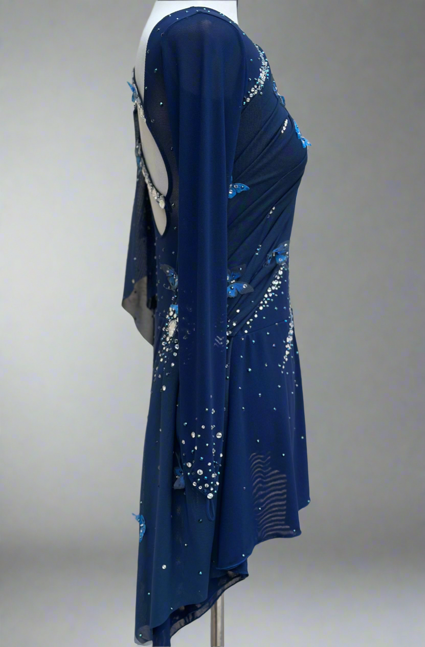 Elegant butterfly figure skating dress in deep blue with crystals, draped design, and open back – sparkle on ice.